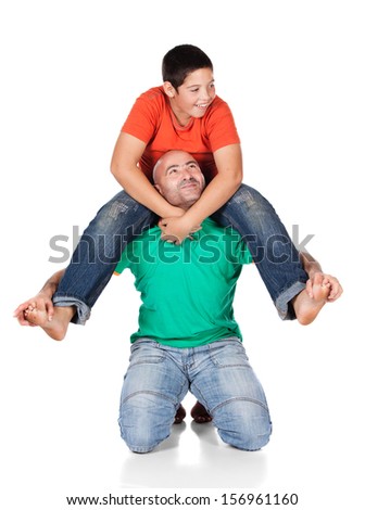 Young caucasian boy wearing an orange t-shirt and blue jeans is playing with his father. The dad is wearing a green shirt. The boy is on the father\'s shoulders.