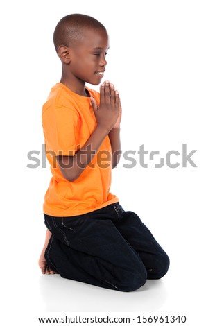 Cute african boy wearing a bright orange t-shirt and dark denim jeans. The boy is kneeling and praying.