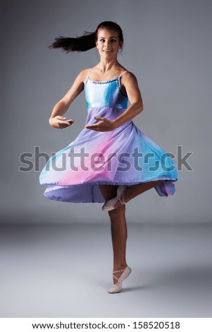 Beautiful female modern jazz contemporary style dancer on a grey background. Dancer is barefoot and wearing a blue and purple dress.