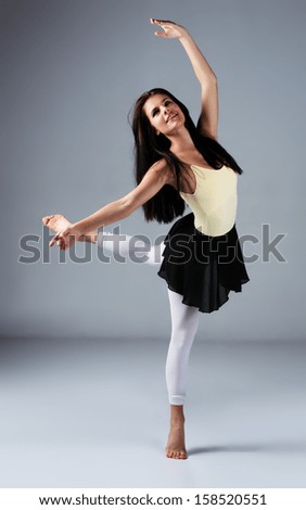 Beautiful female modern jazz contemporary style dancer on a grey background. Dancer is barefoot and wearing a yellow leotard, black skirt and pink stockings.