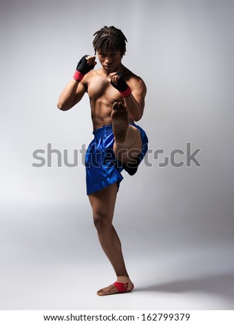 Young muscular athletic male boxer wearing blue boxing shorts and black straps on his hands. Fighter is on a grey background.