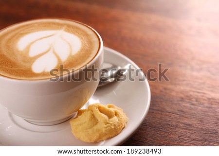 Delicious aromatic cappuccino in a white porcelain cup with a biscuit on the side on a wooden table. Image contains copy space.