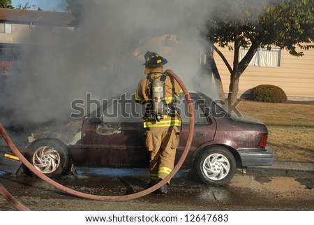 A car caught on fire in the street and firefighters work on putting out the fire.