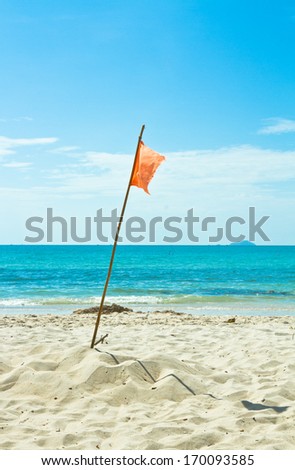 Orange flag on white beach and blue sea