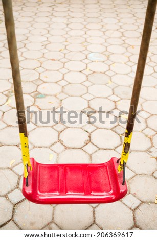 Red swing and rusty iron chain on cement block floor background