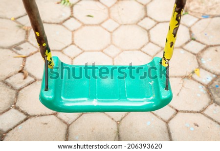 Green swing and rusty iron chain on cement block floor background