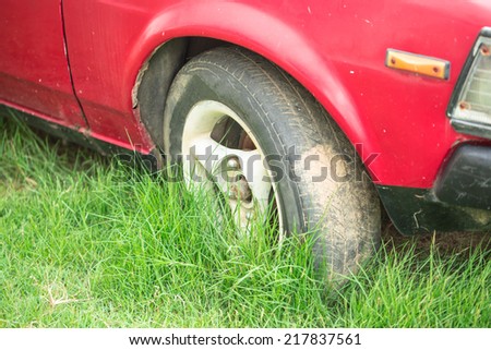 Old red car with flat tire on green yard beside the road