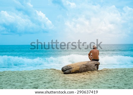Lonely old man sitting on big trunk on strong wave sea beach