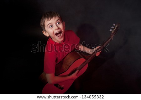 Emotionally singing boy with acoustic guitar on black background