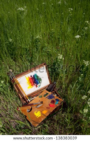 Compact vintage painter\'s case on grass with palette, artistic tools and abstract painting