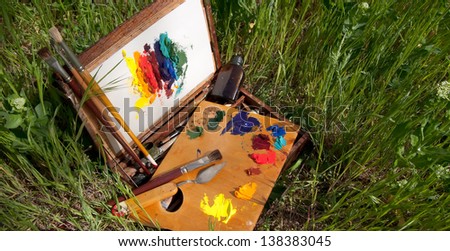 Compact vintage painter\'s case on grass with palette, artistic tools and abstract painting