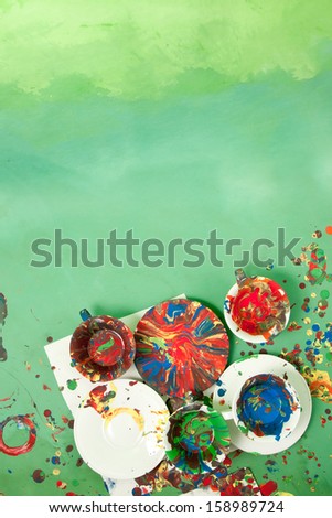 Card with cups with saucers full of bright paints on a green background