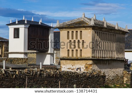 Two Galician granaries with slate roof and pinnacles. One restored and painted white, another unpainted. Next to the house and a slate wall. Rinlo. Lugo. Galicia. Spain