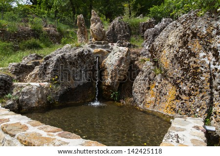 Nice spring or fountain of clear water between rocks jet out and rocks with moss. Water falls to a pylon built with stone wall and surrounded by greenery in spring.La Red. Leon. Spain