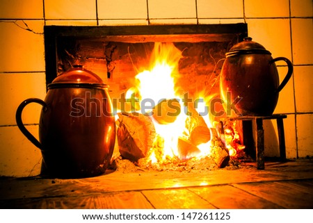 Chimney, kitchen hearth of burning rural house. Fireplace, stove on at home farmhouse. Fireplace, home farmhouse kitchen on. Tint old scene. Cooking pots on trivets two fire