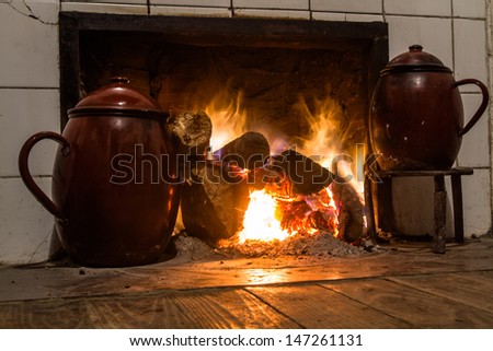 Chimney, kitchen hearth of burning rural house. Ancient scene cooking with two stews in trivet to the fire. Fireplace, stove on at home farmhouse. Scene two ancient cooking pots on trivets fire