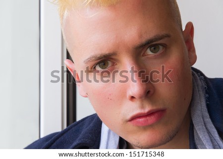 Close up portrait of beardless young man with dyed blond hair and serious expression and contained