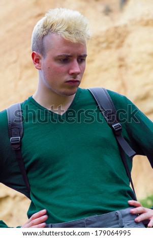 Young caucasian man with dyed blond hair and backpack . Bottom clay cliff