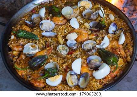 Full red pepper paella cooked on a wood fire at home with shrimp clams and green Padron peppers