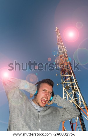 Young Man with Headphones sound or music, with expression of receiving a brutal volume, surrounded by effect of light and antenna or Telecommunications tower