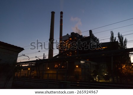 Coal Fired Power Station at Dusk - Coal thermal plant  plant for the production of electricity with chimneys releasing smoke and steam. With the lights on at dusk and railroad tracks in foreground