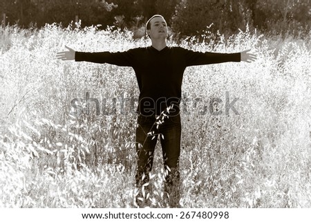 Young Man with Open Arms in Field - Young backlit with arms outstretched in nature and photographic treatment in sepia Man