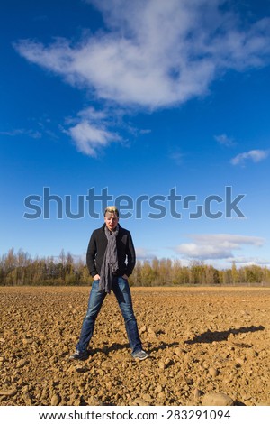 Young sun in a plowed land with trees and blue sky with clouds and angry gesture Man