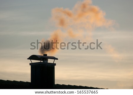 a smoking chimney on the roof of a house in front of the evening sky