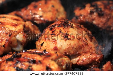 Grilled chicken thighs on a barbecue grill being cooked with seasoning and sauce with smoke rising from charcoal