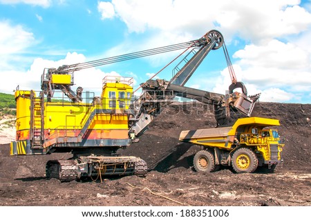 excavator loading lignite stones under cloudy blue sky  in open pit mine