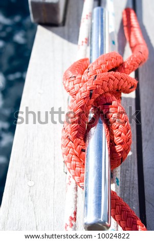 The red rope on the cleat of the sailboat.
