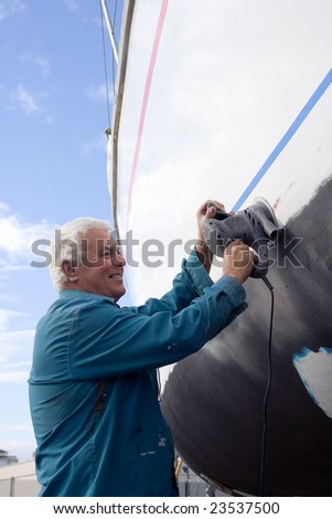 The senior man happy working on the side of a sailboat.