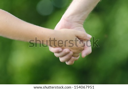 Close-up of two people (man and woman) holding hands on green background. A symbol of love, connection, closeness, relationship and friendship. Natural lightning of summer time.