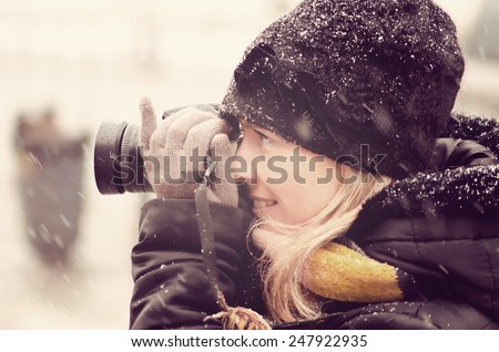 Young pretty  woman photographing outdoor in the winter time. The snow is coming in the background and foreground.