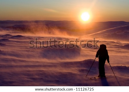 sunset of a sun in the north mountains of Russia in arctic night and persons with a backpack and in ski goes against high wind