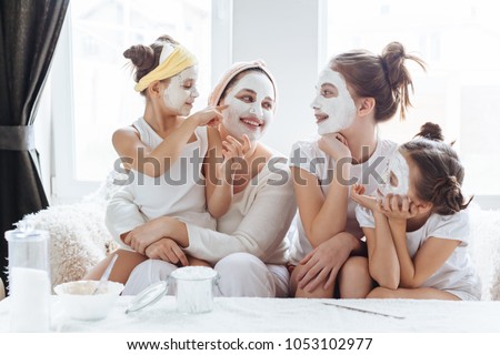 Mom with her daughters making clay face mask. Mother with children doing beauty treatment together. Morning skin care routine.