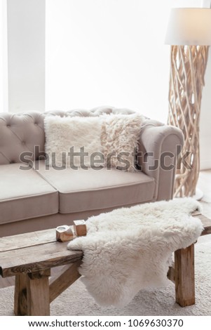 Still life details of nordic living room. Sheep skin rug on rustic bench by the sofa with fur cushions. Cozy winter scene in Scandinavian interior.
