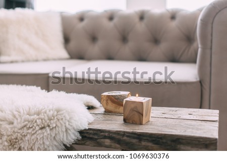 Still life details of nordic living room. Sheep skin rug on rustic bench by the sofa with fur cushions. Cozy winter scene in Scandinavian interior.