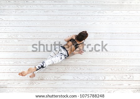 Young beautiful girl wearing fashion sports leggings doing fitness exercise on white wooden flooring in bright gym, top view overhead