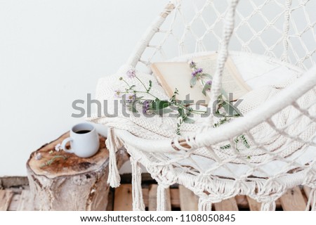 Summer hygge scene with hammock chair, book and flowers. Cozy place for weekend relax in the garden.
