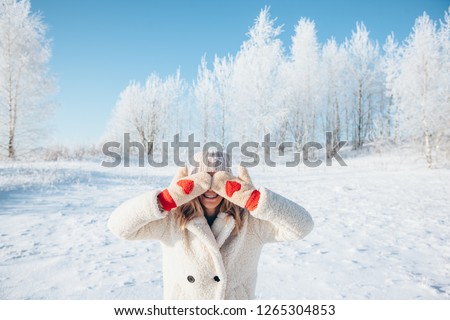 Photo of woman in fur coat and gloves with red hearts closing her eyes over white snow in magic winter day