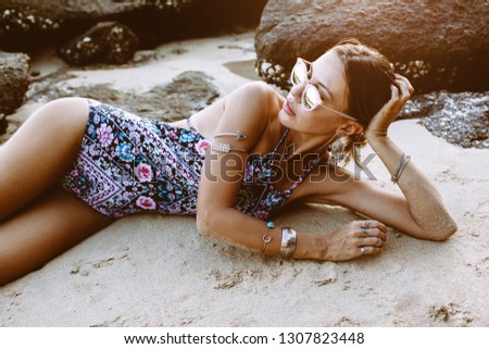 Photo of beautiful boho styled model wearing ethnic swimwear and silver bohemian jewelery on the beach in sunset