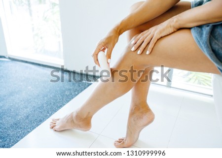 Photo of woman making hair removal on legs with electric epilator. Home depilation after shower.
