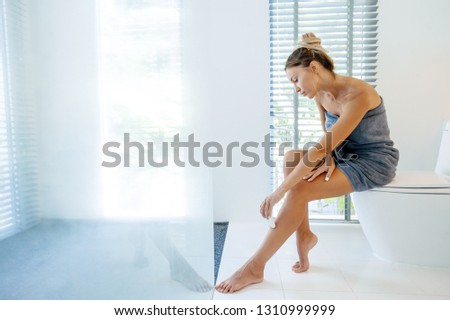 Photo of woman making hair removal on legs with electric epilator. Home depilation after shower in luxury bathroom.