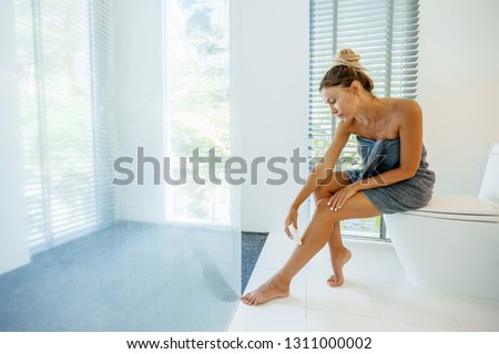 Photo of woman making hair removal on legs with electric epilator. Home depilation after shower in luxury bathroom.