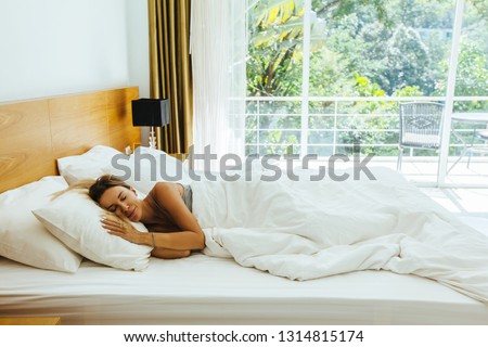 Woman sleeping on bed in luxury hotel room in the morning infront of big window. Chilling well on comfy matress and pillows.