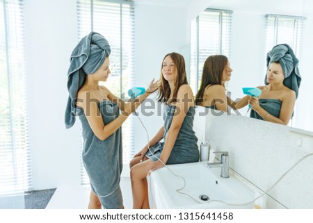 Mom with teenage dauhter making everyday routine in modern hotel bathroom together. Mother is brushing and drying child hair after shower.