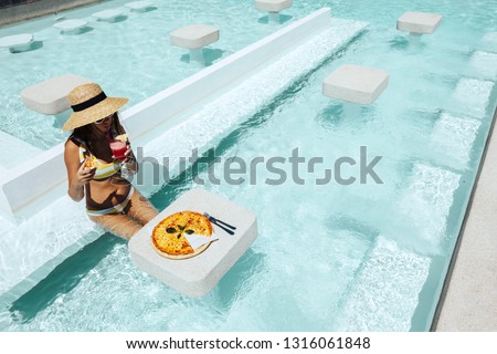 Girl relaxing and eating pizza and drinking cocktail in the hotel pool. Luxury tropical beach lifestyle.