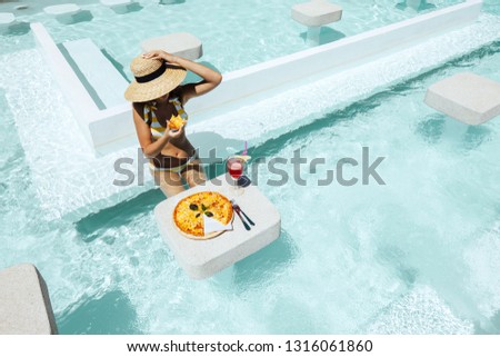 Girl relaxing and eating pizza in the hotel pool. Luxury tropical beach lifestyle.