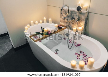 Prepared luxury spa bath decorated with flowers and candles, with wooden tray on it